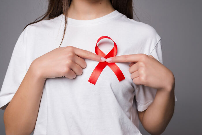Person pointing at a red ribbon on a white shirt, showcasing an American norm.