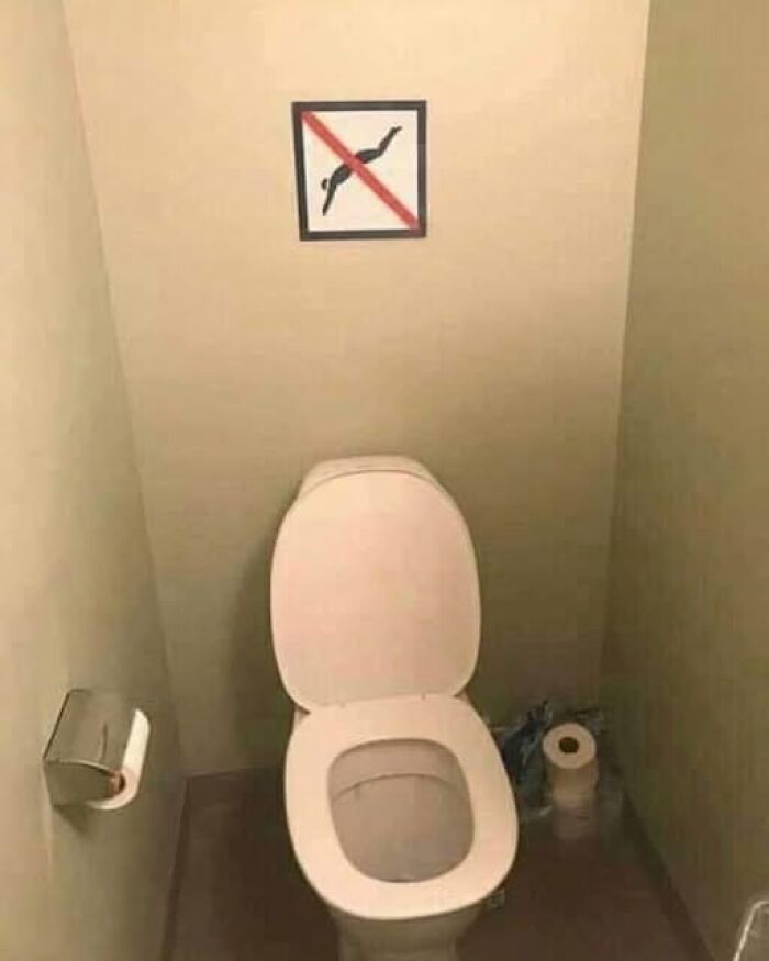 Weird image of a toilet with a no-diving sign on the wall above it.