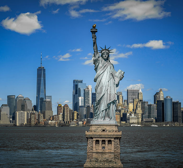 Statue of Liberty with NYC skyline in the background under a clear blue sky.