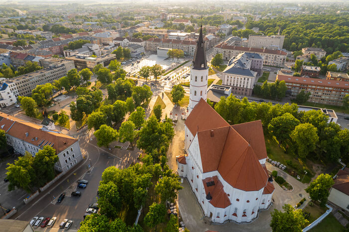 Aerial view of a Lithuanian cityscape with a prominent church surrounded by trees and buildings.