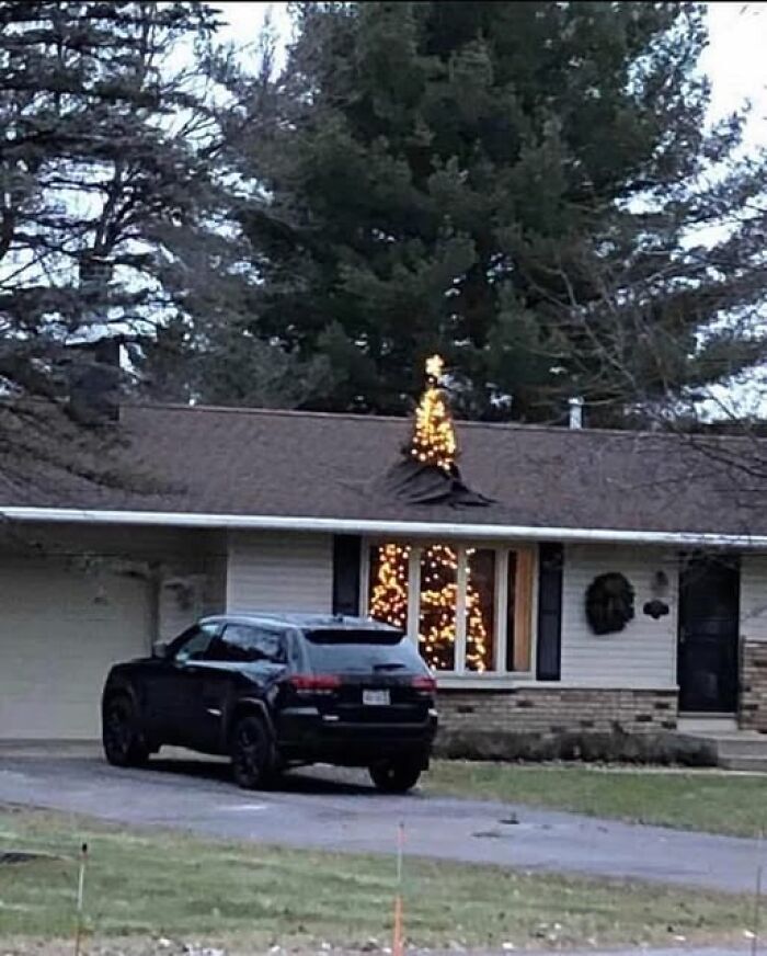 Black SUV parked in front of house with a Christmas tree poking through the roof, showcasing a weird image in the scene.