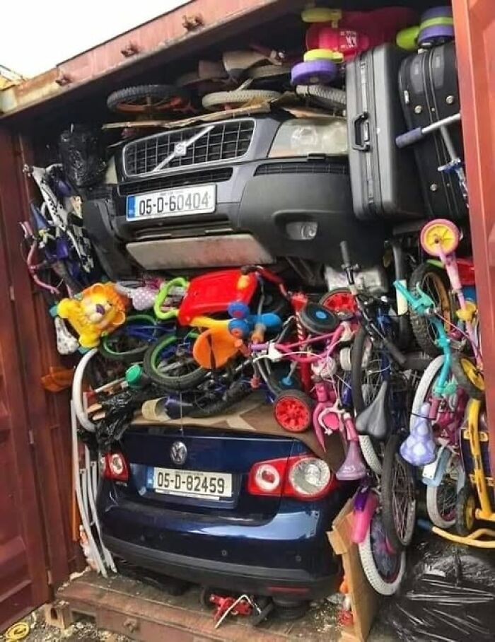 Weird image of a packed shipping container filled with cars, bicycles, and assorted items.