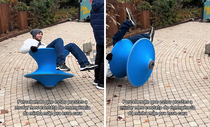Man balancing on a blue spinning seat, playfully struggling in a public outdoor area.
