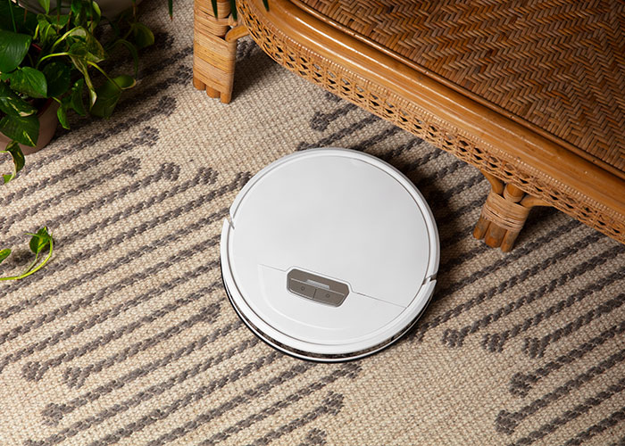 Robotic vacuum cleaning a carpet near a wicker chair, adding a whimsical touch to home chores.