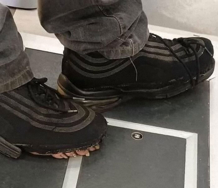 Weird shoes with toes peeking out from under, worn with gray jeans on a tiled floor.
