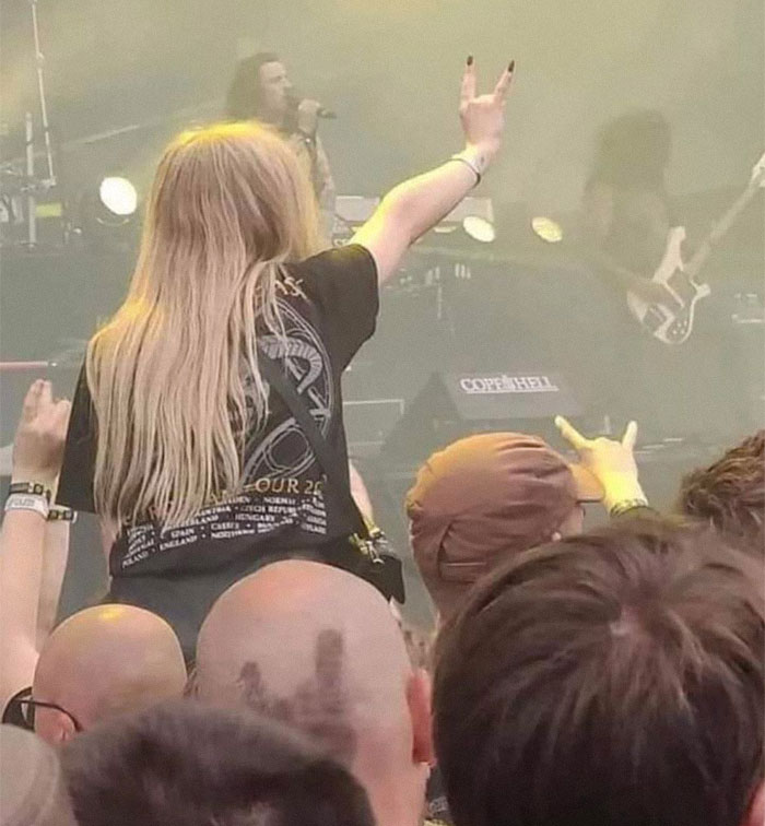 Persona en un concierto levantando la mano en señal de rock, rodeada de gente emocionada. Imágenes raras en un evento musical.