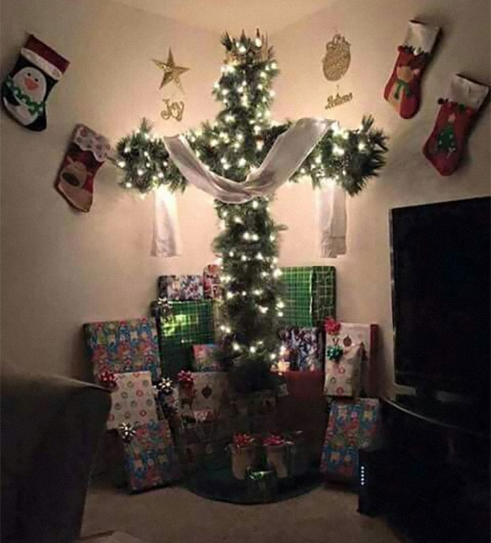 Weird image of a cross-shaped Christmas tree with lights and presents beneath in a festive room.