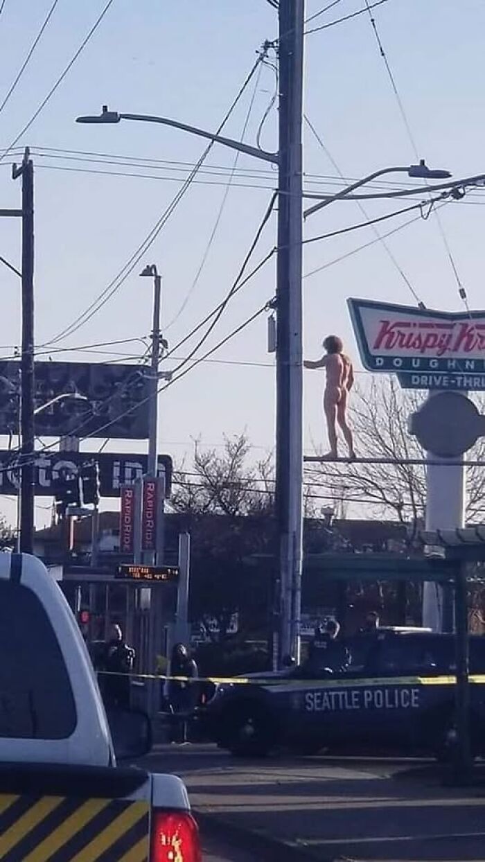 Weird image of a person on utility pole near Krispy Kreme and Seattle police car on the street below.