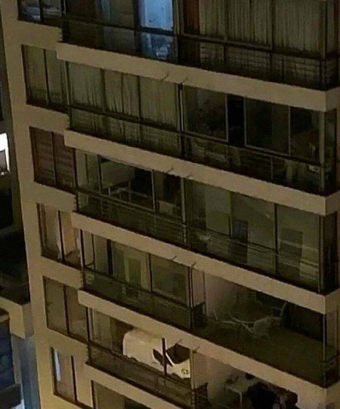 Apartment building with a van parked on the balcony, showcasing a weird image worth seeing.