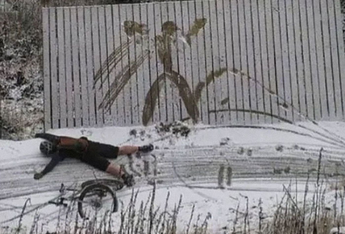 Persona con bicicleta caída en la nieve junto a un dibujo cómico. Imagen rara que destaca en la escena invernal.