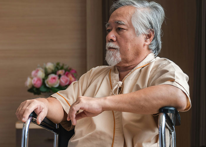 Elderly man in a wheelchair, contemplating, with flowers in the background.
