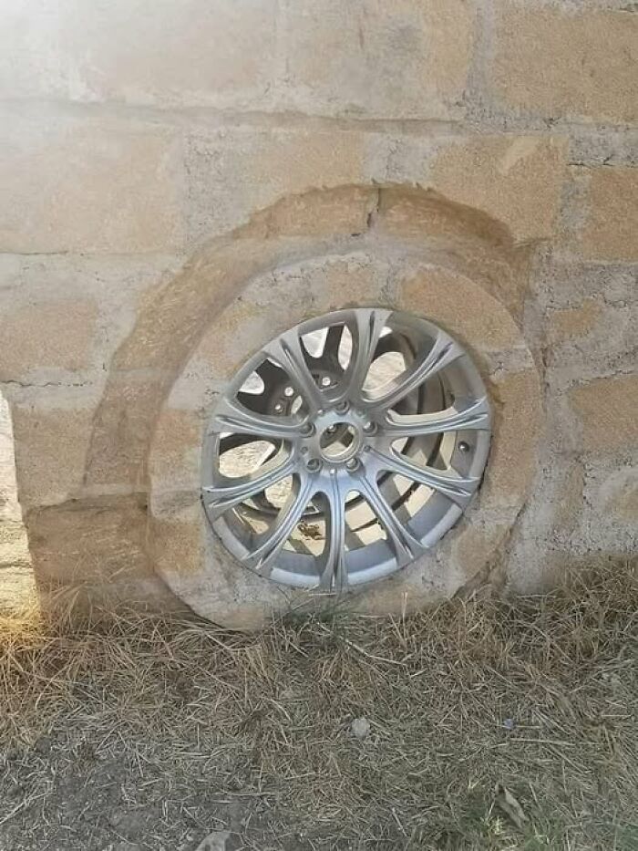 A car wheel embedded into a brick wall, illustrating a weird and unconventional architectural choice.