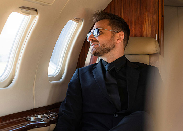 Man in suit and sunglasses sits confidently in a plane, embodying themes of carefulness and potential revenge.