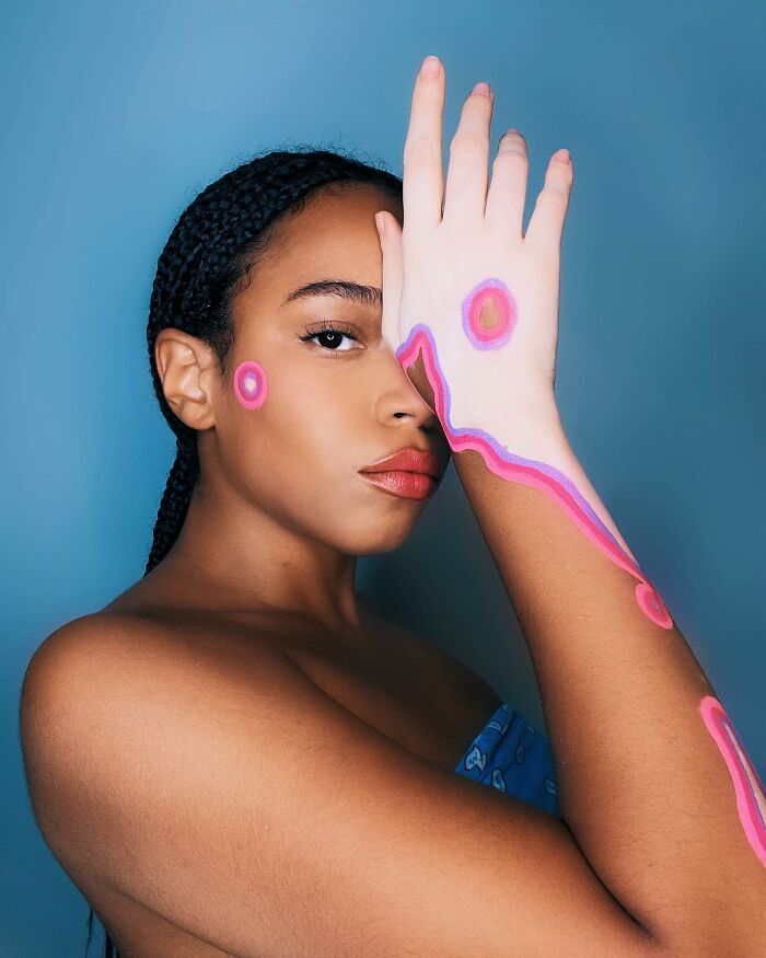 Woman with vitiligo shows body art in pink against a blue background, highlighting beauty and self-acceptance.