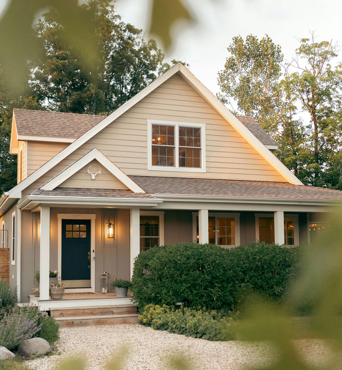 Charming cottage-style house with a front porch and warm lights, surrounded by greenery, conveying a rich, serene lifestyle.