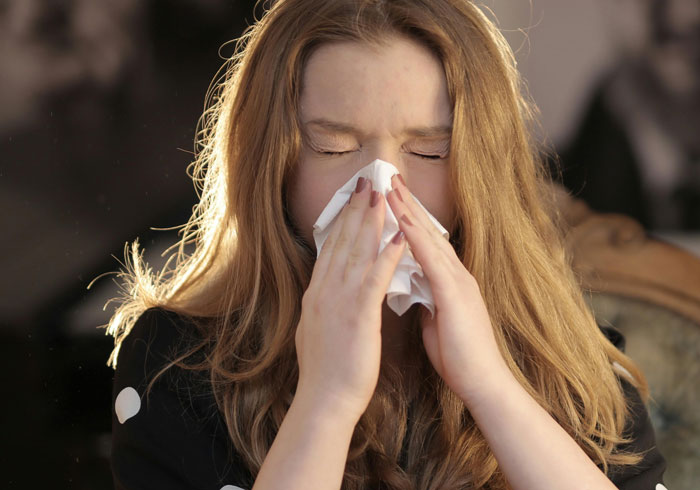 Joven estornuda con un pañuelo en las manos, divertida situación de estudiante en clase.