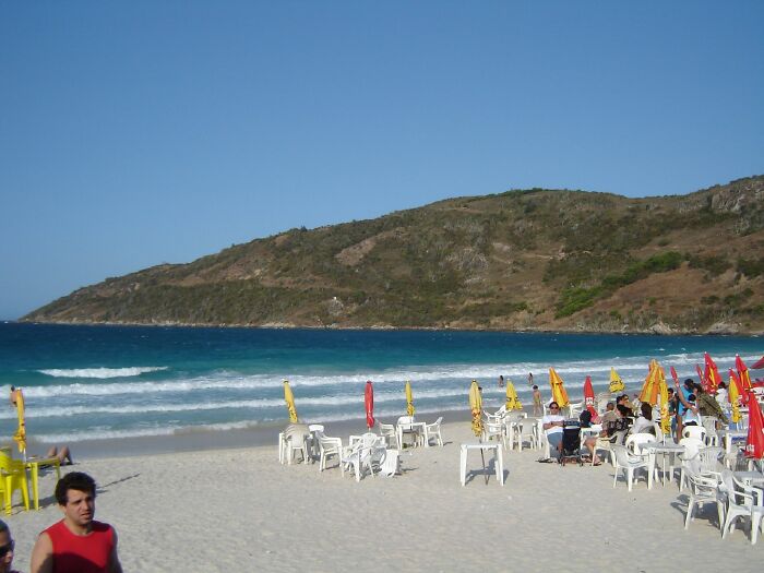 Retro Brazilian beach scene with sun umbrellas and empty chairs on the sand, waves in the background.