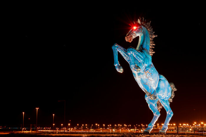 Blue sculpture of a rearing horse with glowing red eyes at night, related to inventors' creations.