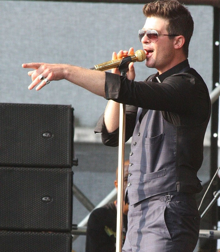 Singer performing on stage with a gold microphone, wearing sunglasses and a vest, highlighted in a discussion about singers.