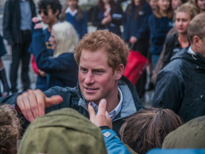 A celebrity interacting with fans outdoors, surrounded by a crowd in a rainy setting.