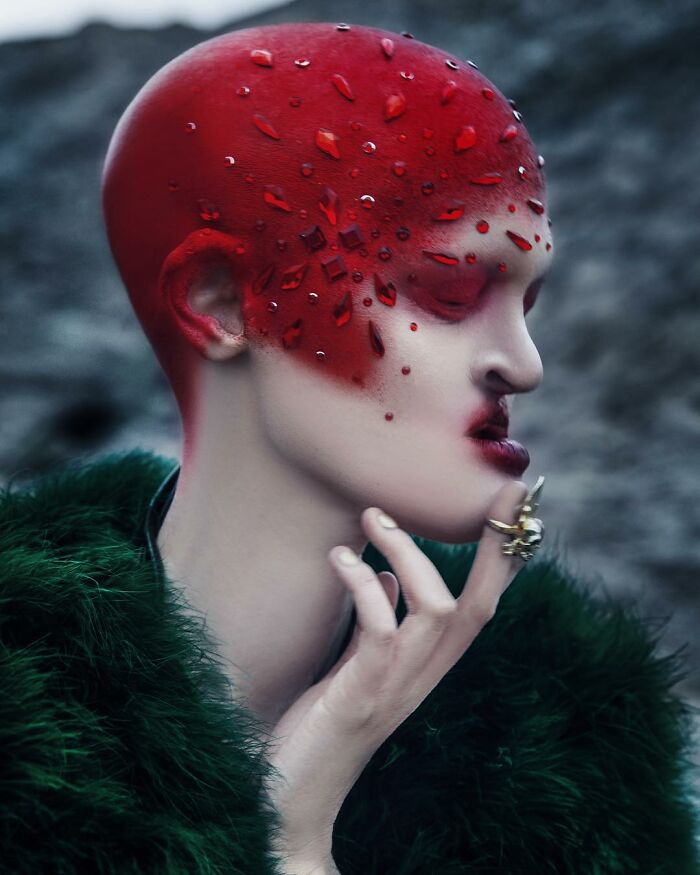 Unique model with a striking red and jeweled headpiece, wearing a green fur garment in a dramatic pose.