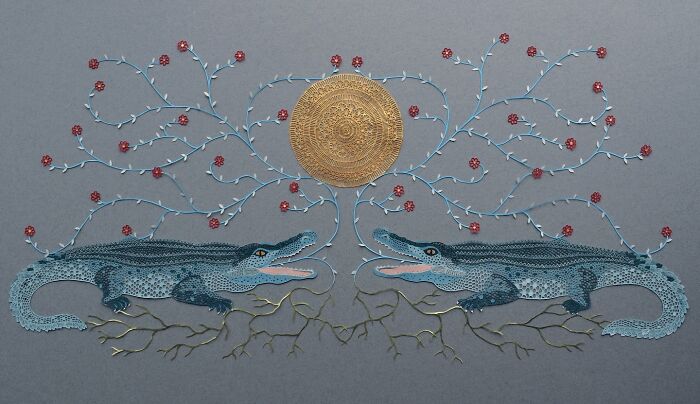 Intricate paper art design featuring two crocodiles with swirling branches and a circular sun motif in the background.