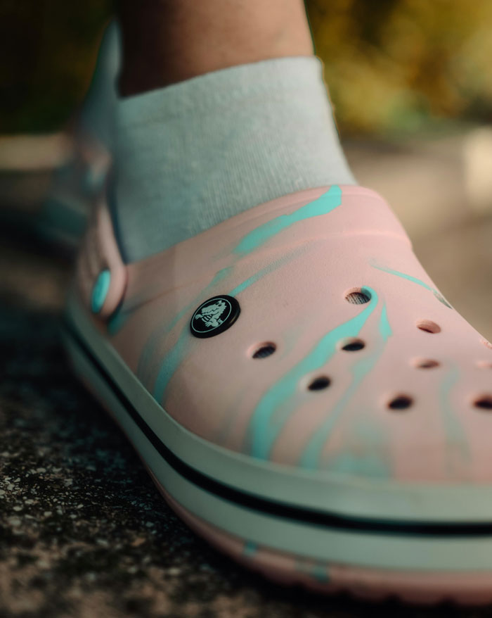 Close-up of a pink Croc shoe with light blue accents on a textured surface, illustrating humorous student moments.