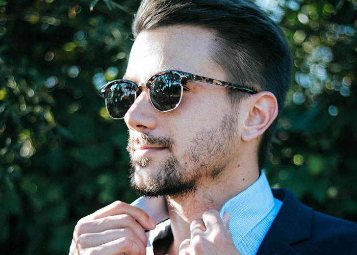 Man adjusting collar in sunglasses, representing confidence and revenge mindset against bosses.