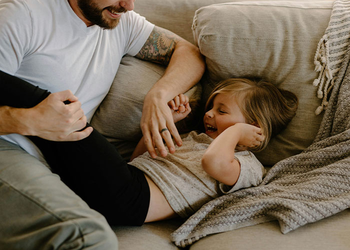 A father and child sharing a heartfelt moment, laughing together on a cozy couch.