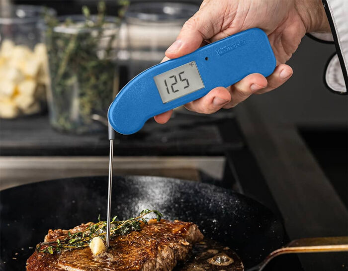 A blue meat thermometer reading 125°F inserted into a steak, showcasing beautiful design and durability.