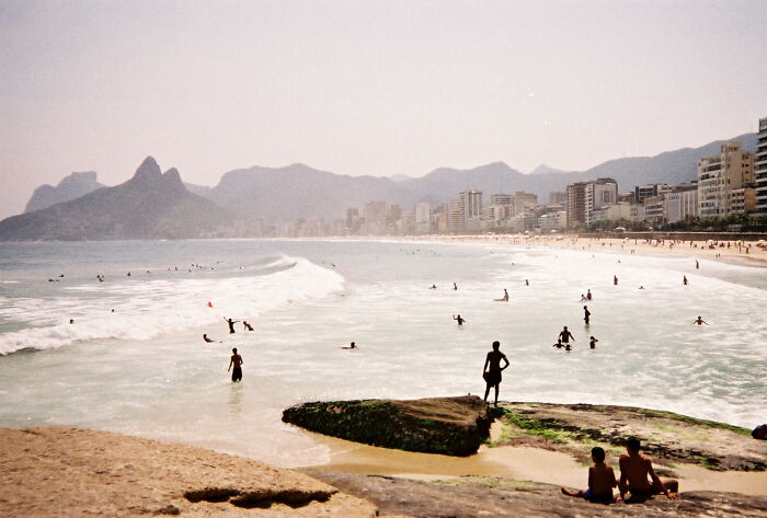 Retro Brazilian beach scene with people enjoying the sun and waves along a scenic coastal view.