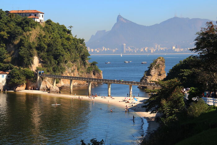 Retro Brazilian beach scene with sunlit sand, people relaxing, and lush greenery under a clear blue sky.