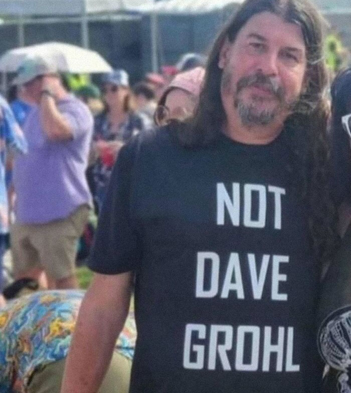 Hombre con camiseta divertida en un evento al aire libre, desmentiendo identidad con humor.