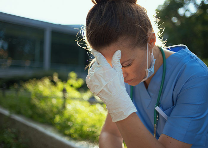 Nurse in scrubs looking stressed, reflecting on heartfelt last words from dying patients in a garden setting.