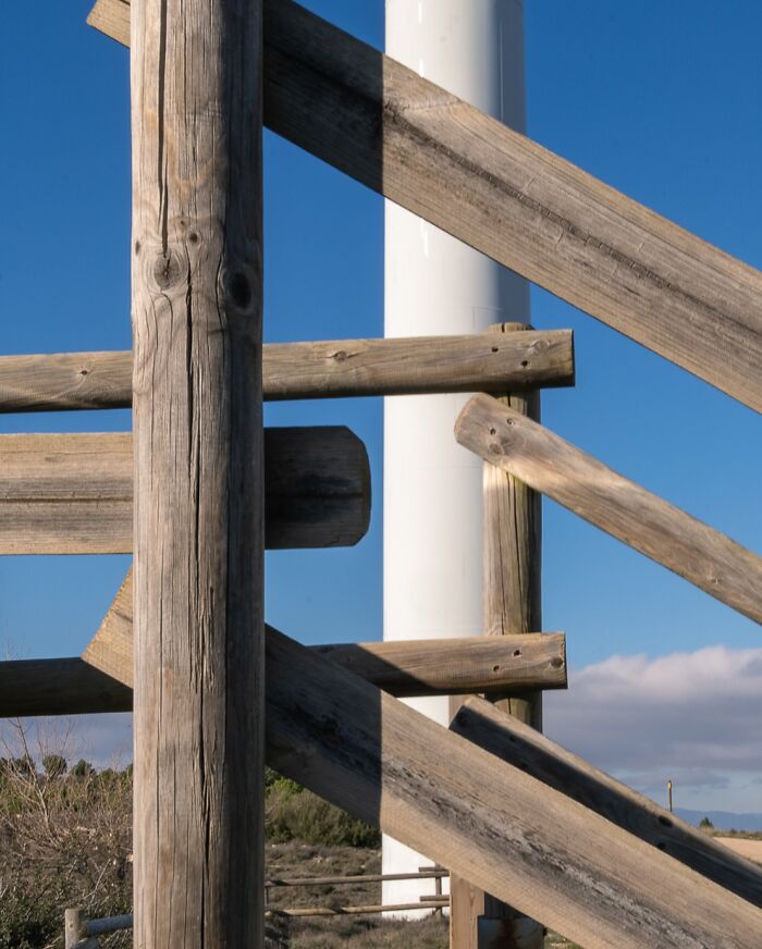 Wooden beams aligning with a wind turbine against a blue sky, part of the Coincidence Project photos.