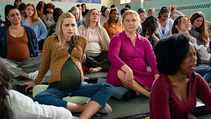 Pregnant women sitting on a gym floor, including Amy Schumer, during a prenatal class in a Netflix movie scene.