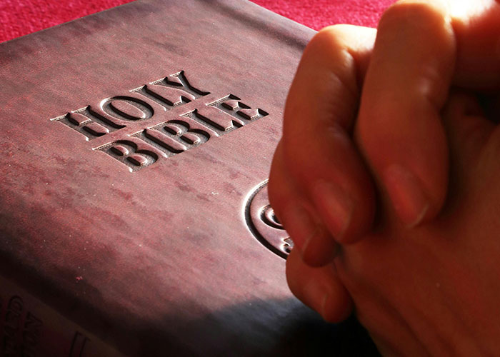 Hands clasped in prayer on a Holy Bible, reflecting American cultural nuances in Europe.