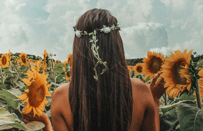 Woman in a sunflower field, adorned with a floral headpiece, symbolizing the "prettiest girl" theme.