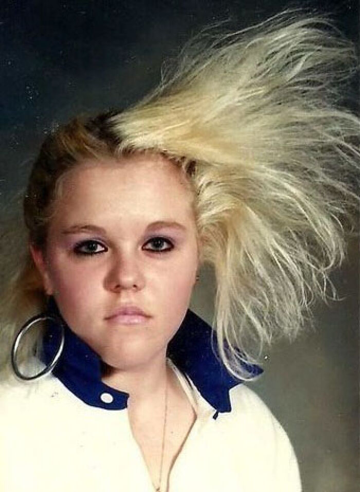 80s hair disaster with blonde, voluminous style and large hoop earrings, embodying iconic fashion of the era.