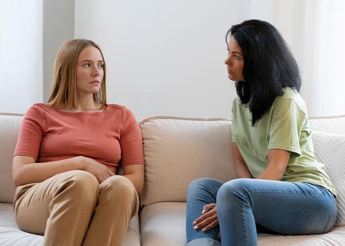 Two women sitting on a couch, having a serious conversation about being late. Two women sitting on a couch, having a serious conversation about being late.