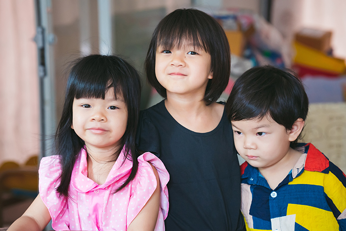Three young children smiling and posing indoors, showcasing family bonds.
