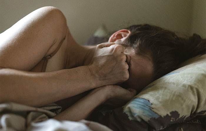 A woman lying in bed, covering her face with her hands, reflecting on a personal moment about divorce papers and relationships.