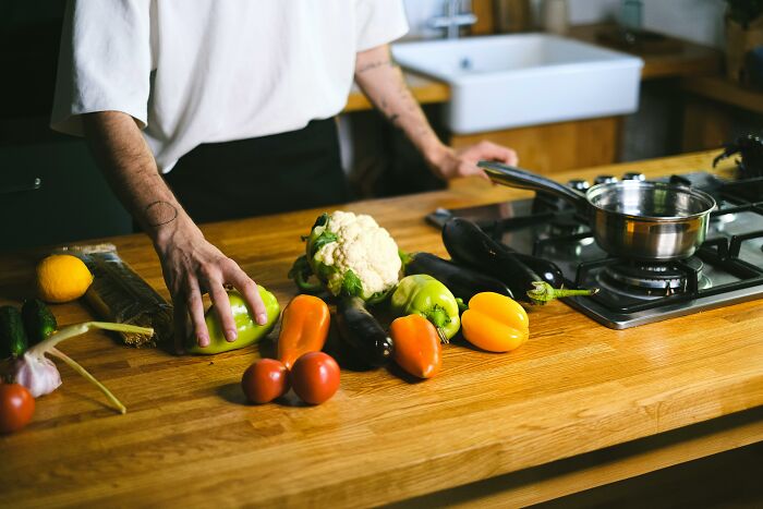 Person organizing fresh vegetables on a wooden kitchen counter, illustrating things associated only with rich people.