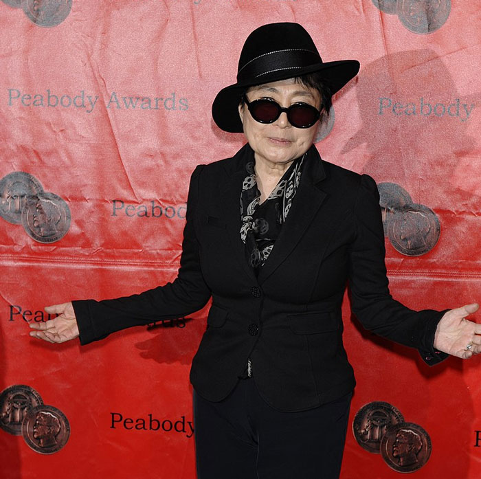 Singer in black outfit and sunglasses at Peabody Awards backdrop.