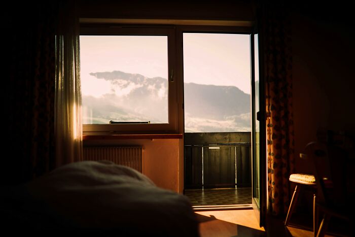 View of mountains through open balcony door, with warm sunlight enhancing a cozy room setting.