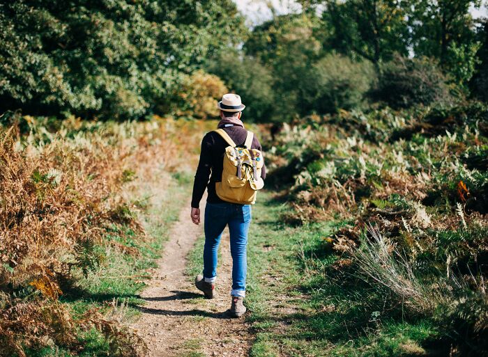 Man walking on a trail with a yellow backpack, surrounded by greenery, illustrating fitness myths outdoors.