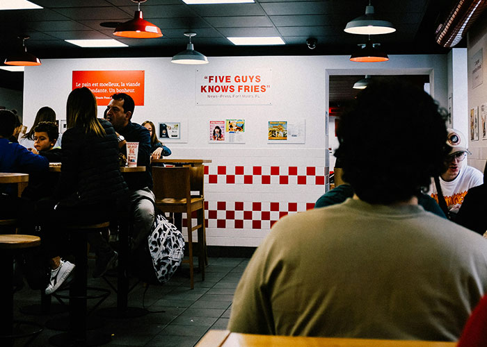 People sitting in a Five Guys restaurant, highlighting aspects of being overweight in a casual dining environment.