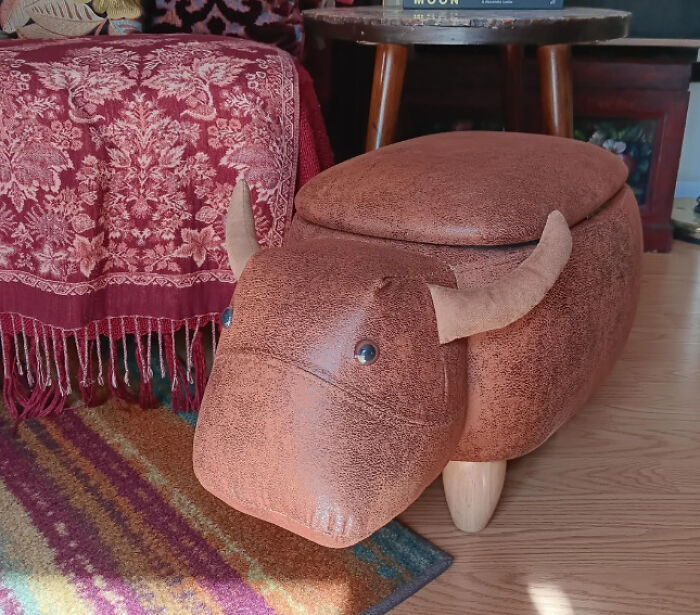 Unique bull-shaped footstool found while thrifting, placed next to a red blanket on a patterned rug.