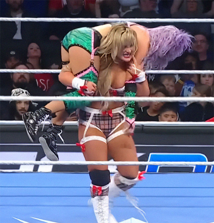 WWE star in the ring, wearing a plaid and green outfit during a live match. WWE star in the ring, wearing a plaid and green outfit during a live match.