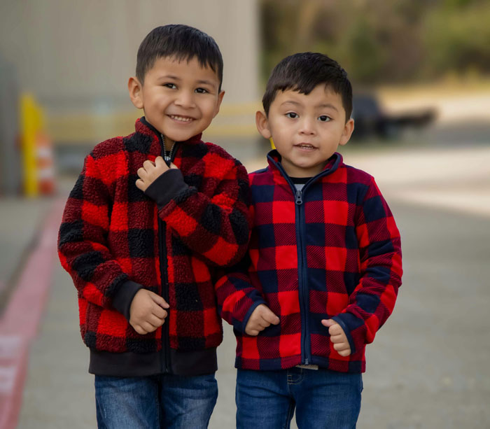 Two young boys in plaid jackets standing side by side, smiling outdoors, illustrating funny things students say.